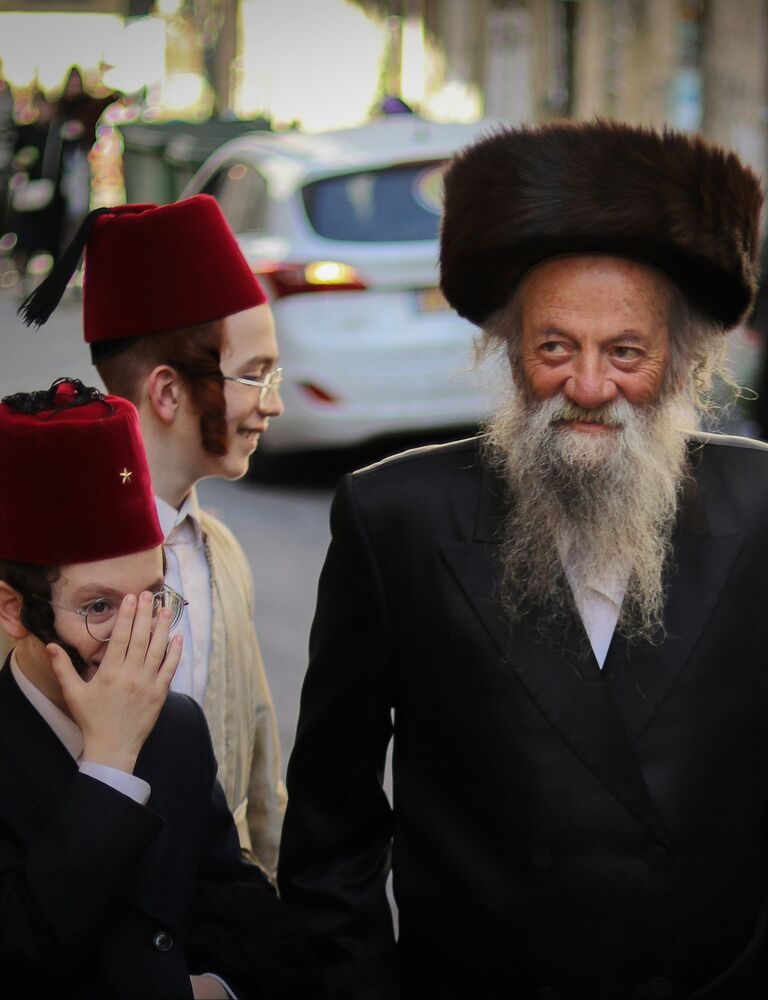 man with shtreimel in street on purim next to two young boys with fez hats