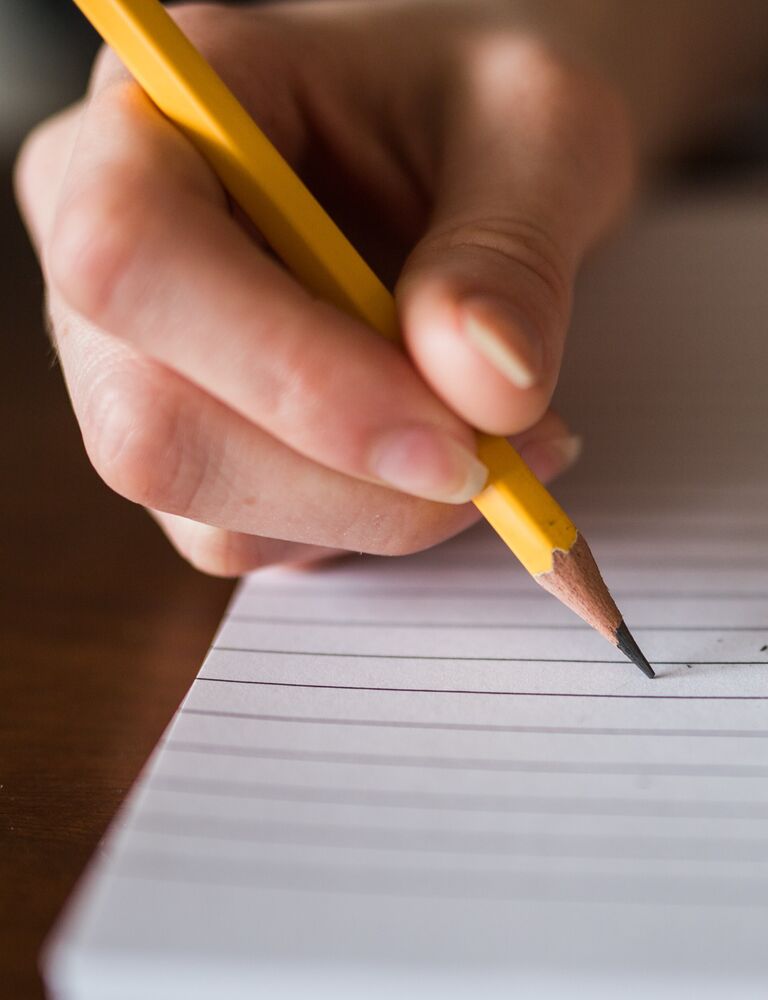 person's hand writing notebook with pencil 