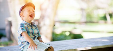 young boy sitting on table laughing and holding a book